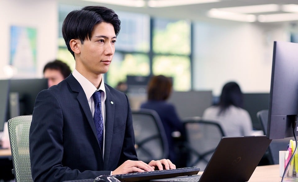 自席でノートパソコンをタイピング中の石井さん。モニタを真剣な表情でみている