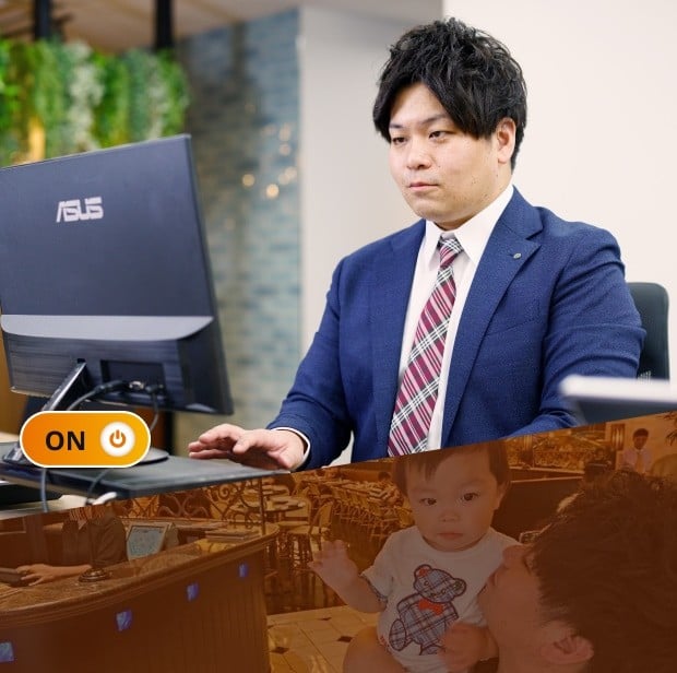 勤務中の久保さん。オフィスの自席で正面を向いて座り、デスクトップPCをタイピングしているシーン。明るい紺のスーツに赤のチェック柄ネクタイで真剣な表情。ON/OFFで言うところの「ON」状態