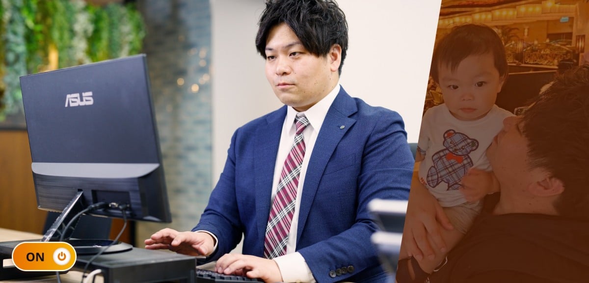 勤務中の久保さん。オフィスの自席で正面を向いて座り、デスクトップPCをタイピングしているシーン。明るい紺のスーツに赤のチェック柄ネクタイで真剣な表情。ON/OFFで言うところの「ON」状態