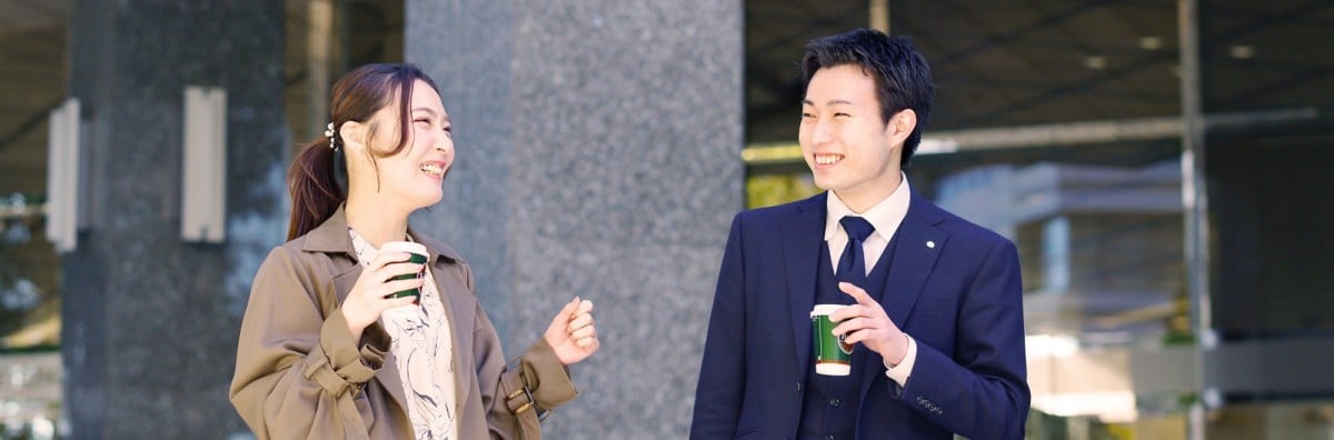 屋外でコーヒー片手に笑顔で会話中の2人