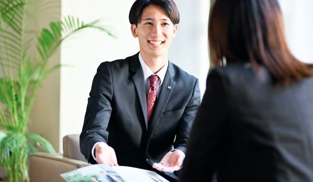 応接室で書類を見ている相手に笑顔で話すスーツ姿の男性の写真
